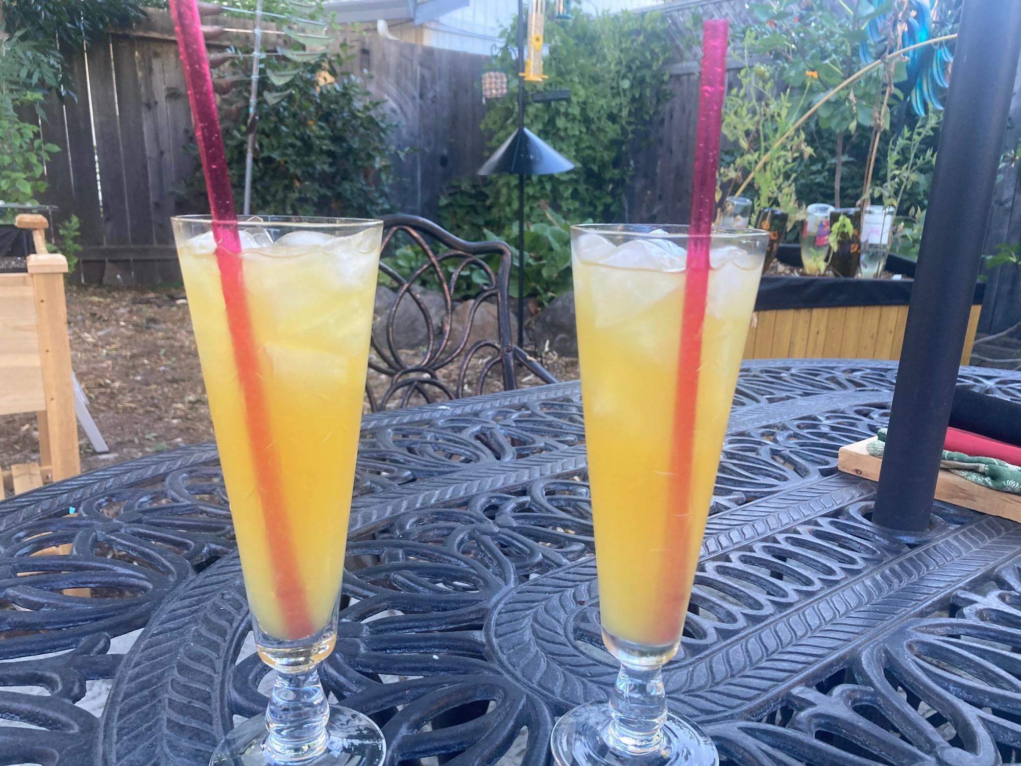 Two footed sling glasses filled with ice, an orange cocktail, and red straws