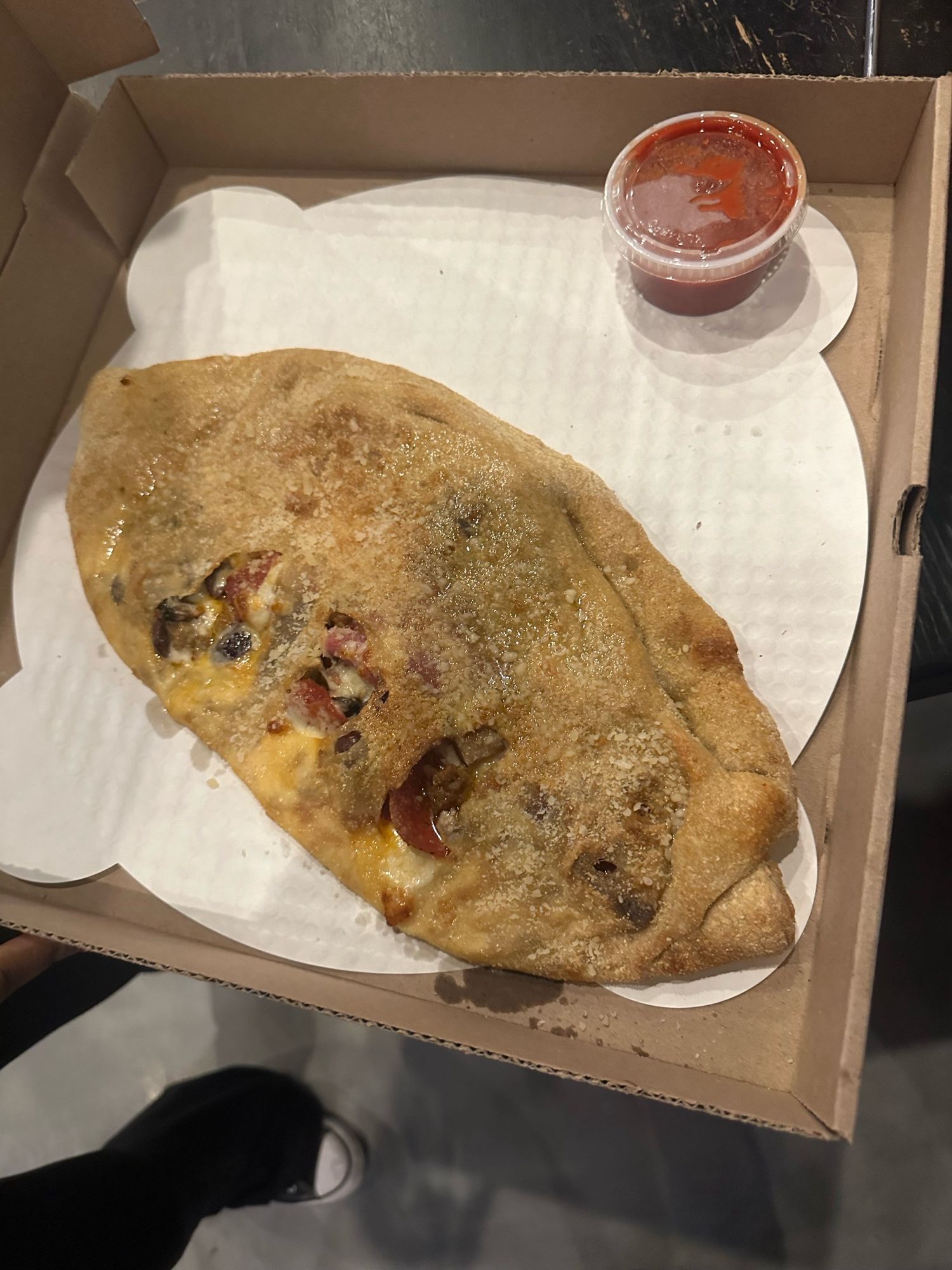 A calzone filled with meats (pepperoni, salami, bacon), ham, Kalamata olives, and portobellos