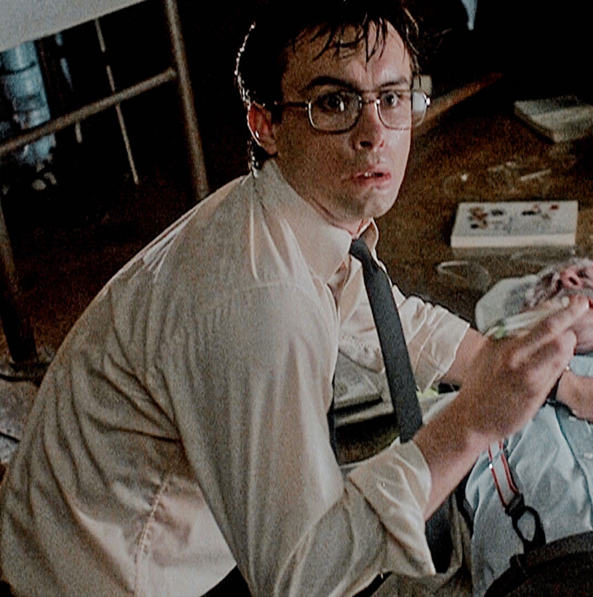 Jeffrey Combs as Herbert West in the 1985 adaptation of Re-Animator (best version). A young man in a slightly oversized white button up and a black tie with large glasses, incredibly sweaty and in a very startled hunched over position. Upon further inspection he's crouched over a dead body but still managing to look like the victim.