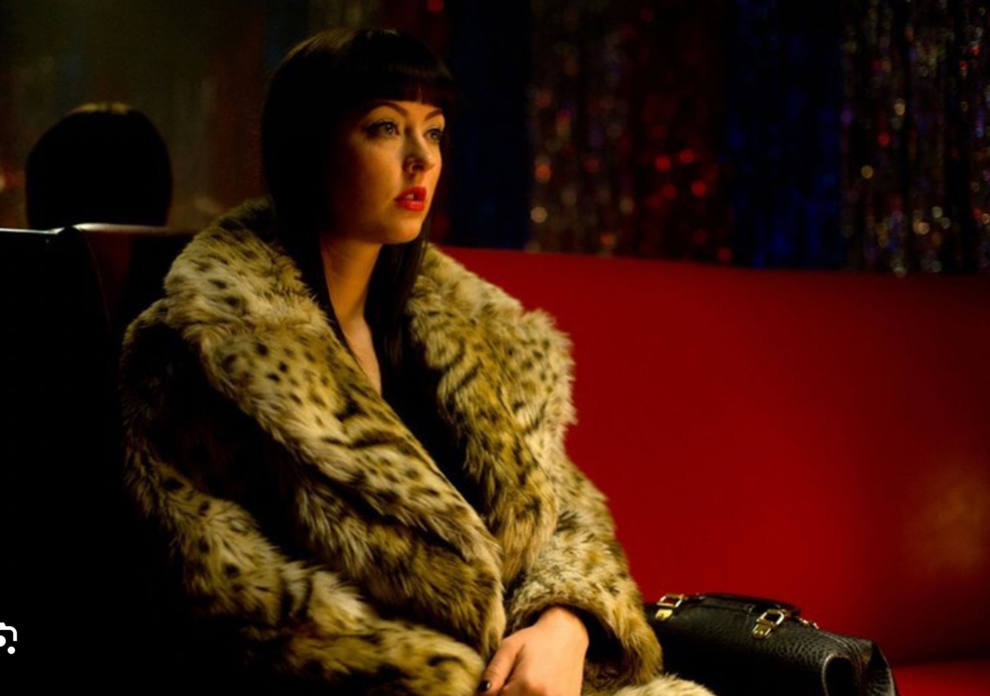 Katherine Isabelle as American Mary (from 2012 film of same name) wearing an oversized fur coat and red lipstick, possibly dissociating.