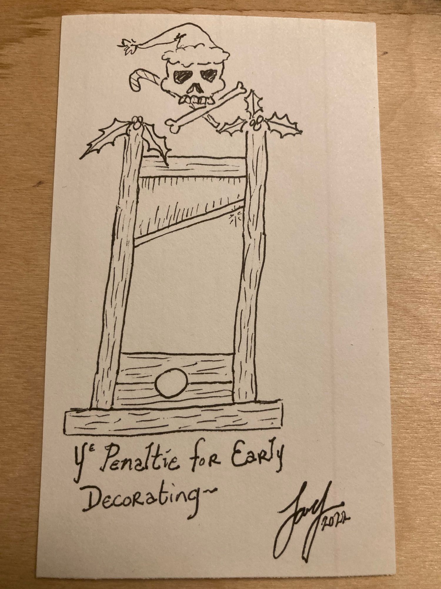 A cartoon of a guillotine decked with boughs of holly, and topped with a skull in a Santa hat above a crossed bone and candy cane. Caption reads “YE PENALTIE FOR EARLY DECORATING” in an old-timey hand. It is signed and dated “Jay 2022” and was a response to premature revelry.