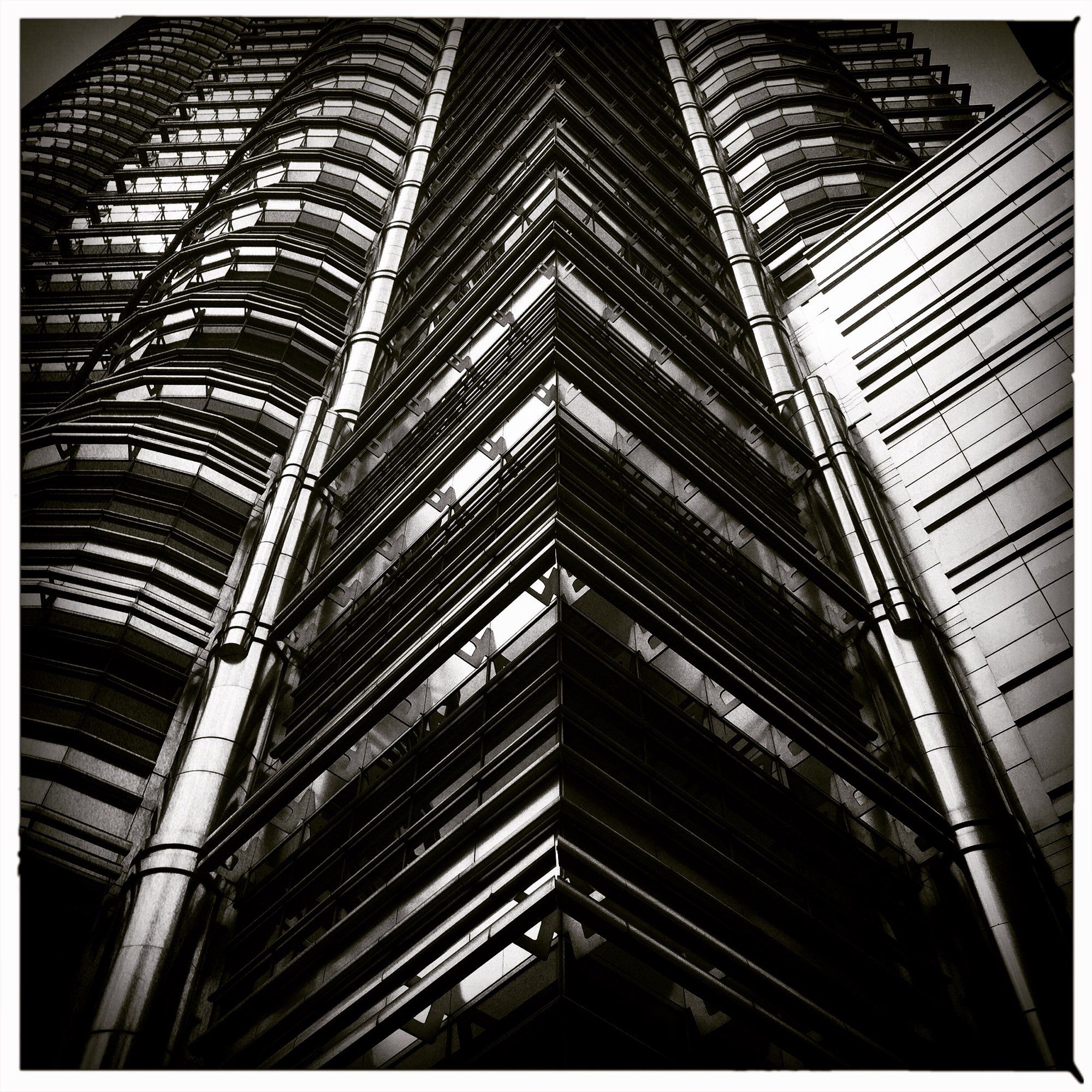 Photo. Black and white close crop of one of the two Petronas Towers, in Kuala Lumpur, with deep black shadows and vignette.