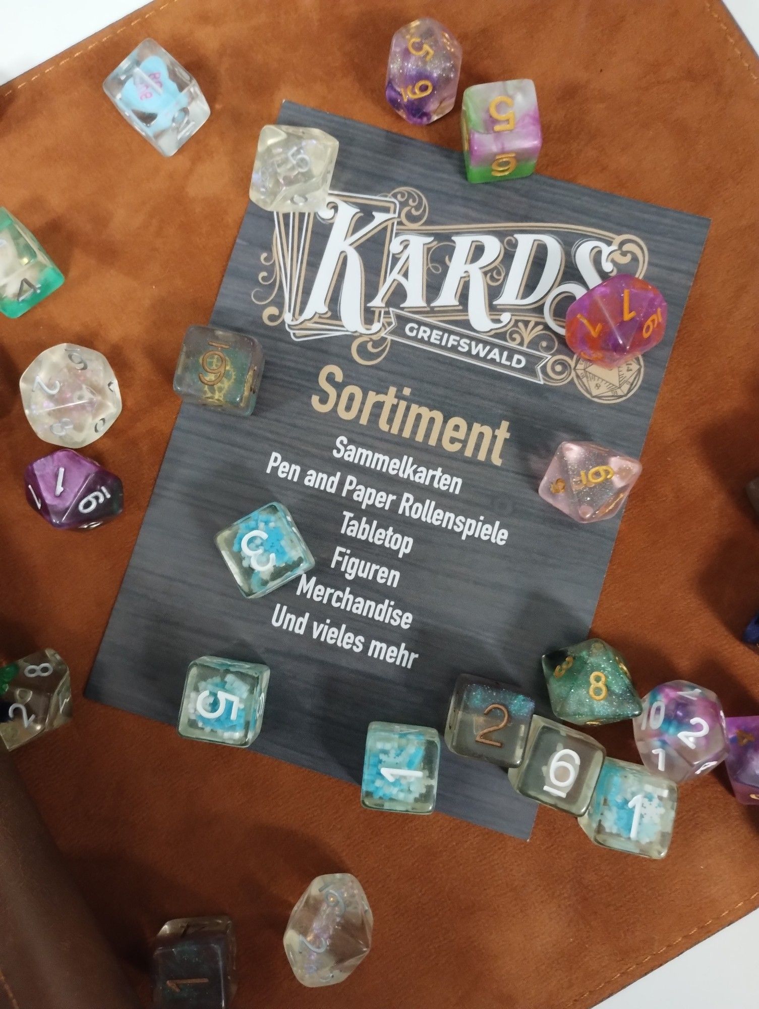 Flyer mit Würfeln. Text auf dem Flyer "KARDS Greifswald Sortiment: Sammelkarten, Pen and Paper Rollenspiele, Tabletop, Figuren, Merchandise, und vieles mehr"