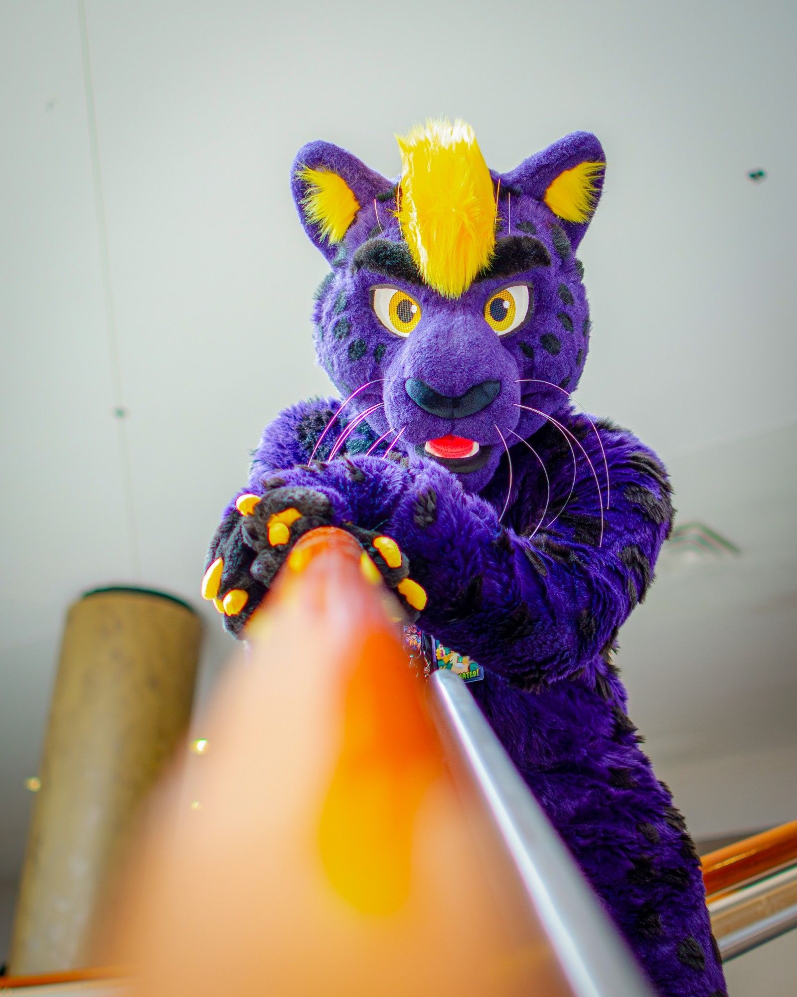 A purple and yellow fursuiter leaning against a stair railing