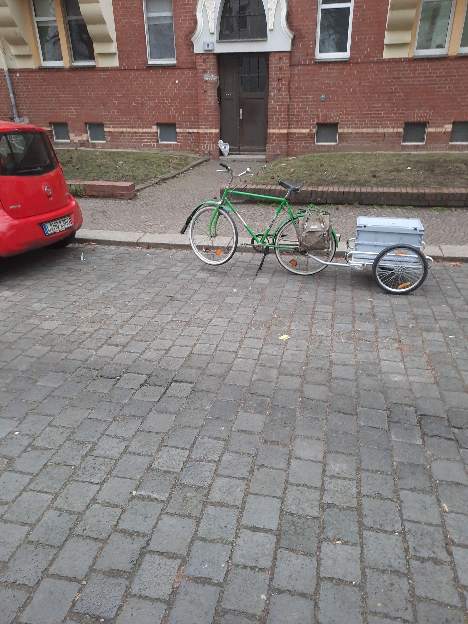 ein grünes mifa "DDR" fahrrad mit Anhänger steht in einer Parklücke am Straßenrand. links im Bild das Heck eines roten autos