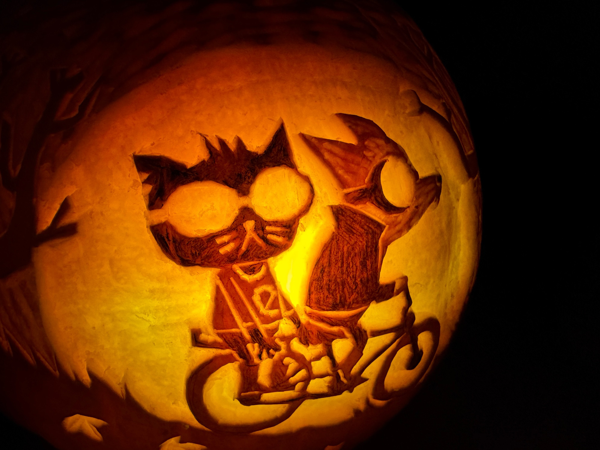 A close up of a lit Halloween pumpkin carved with an image from the game Night in the Woods, showing Gregg and Mae riding a bike