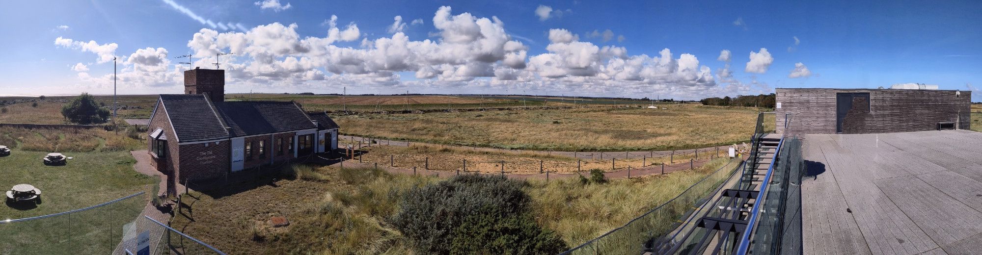 A panoramic view from the visitor centre at Gibraltar Point showing the picnic ares, the old coastguard station, salt marsh and the masts of the nearby sailing club and agricultural land beyond.