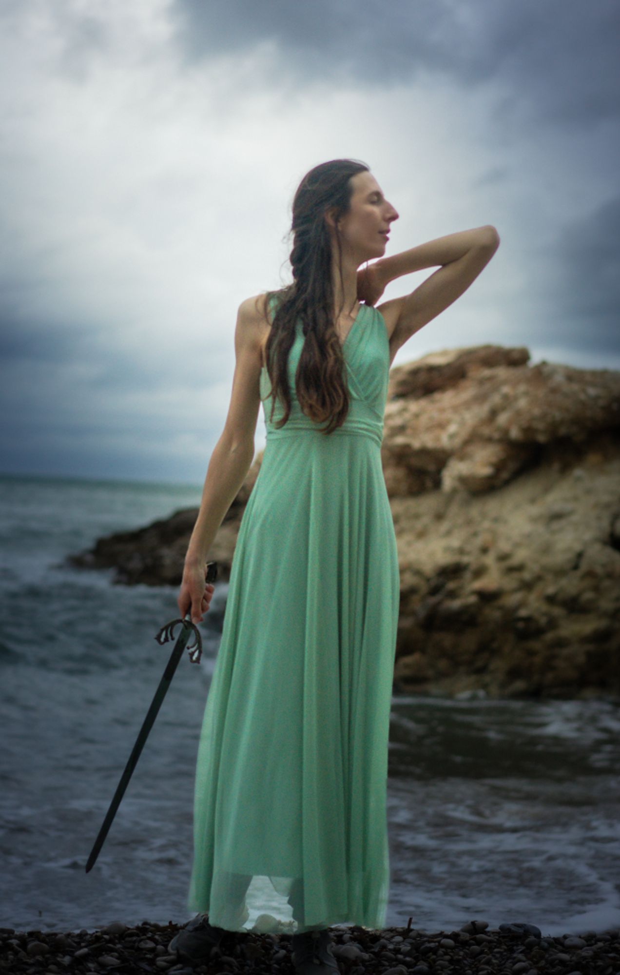 Photo of a woman on the coast, in a green dress, holding a sword