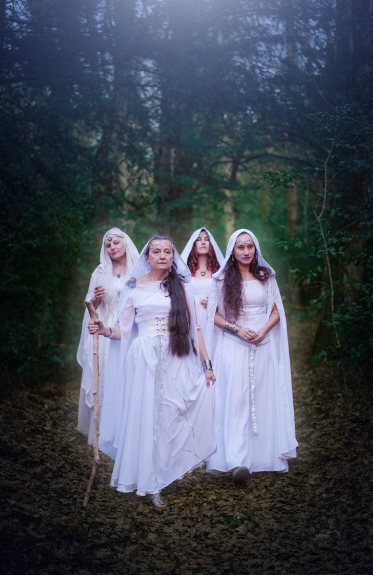 Photo of four elf women walking on a forest path. A glow comes out of them.