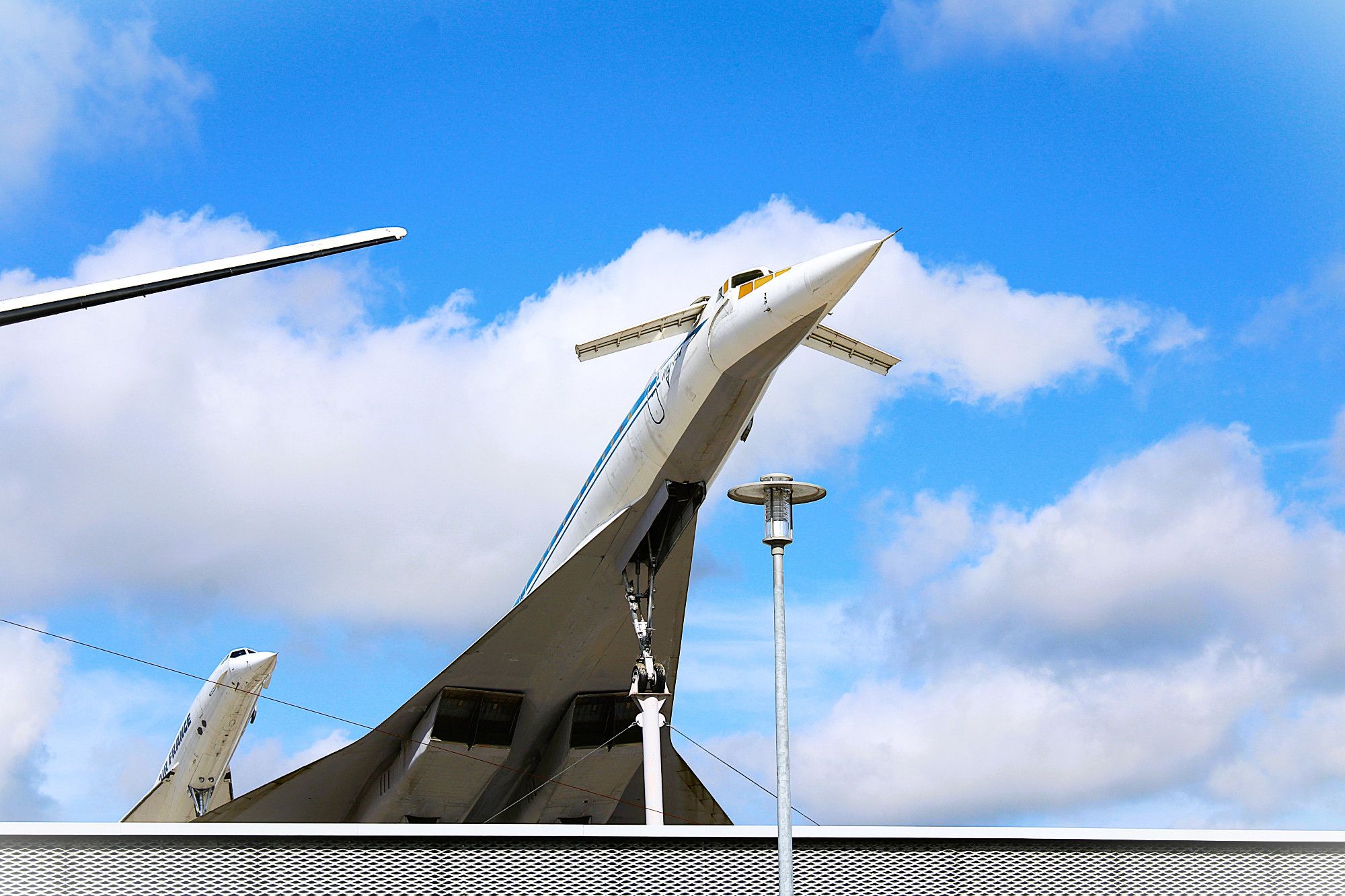 Ein heller sonniger Tag mit blauem Himmel und weißen Wolken. Aus der Froschperspektive sieht man eine Tupolev Tu-144  vorne rechts, hintan links die Concorde F-BVFB.