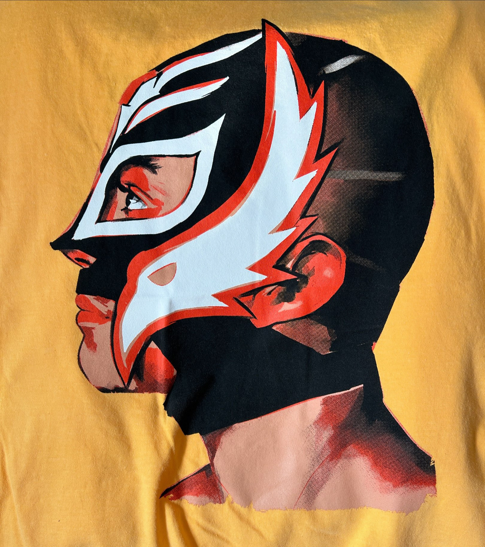 Portrait of Rey Mysterio screenprinted on a light yellow/orange shirt.