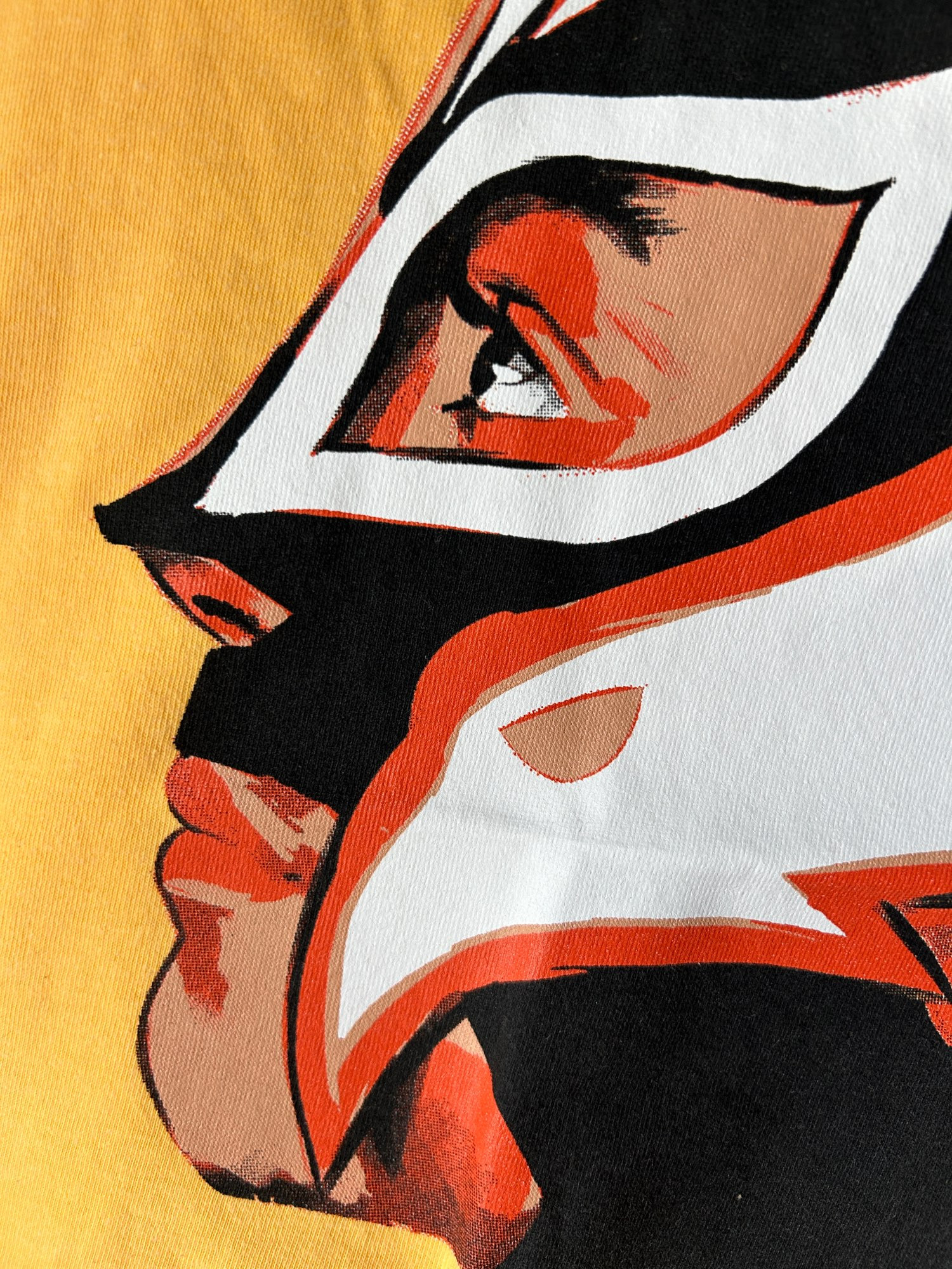 Portrait of Rey Mysterio screenprinted on a light yellow/orange shirt.