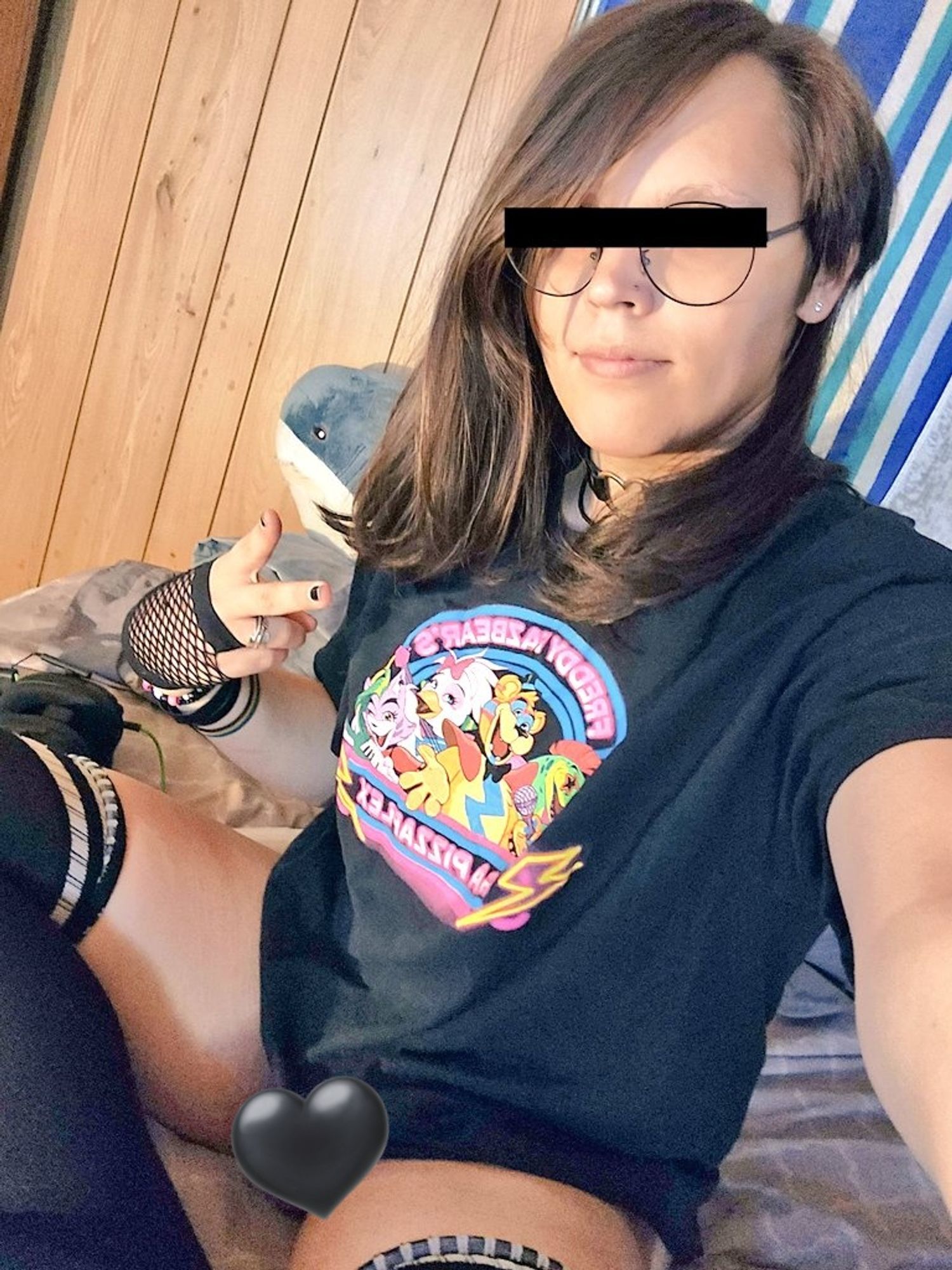 A woman posing in bed with fishnet gloves, a FNAF shirt, and thigh highs.