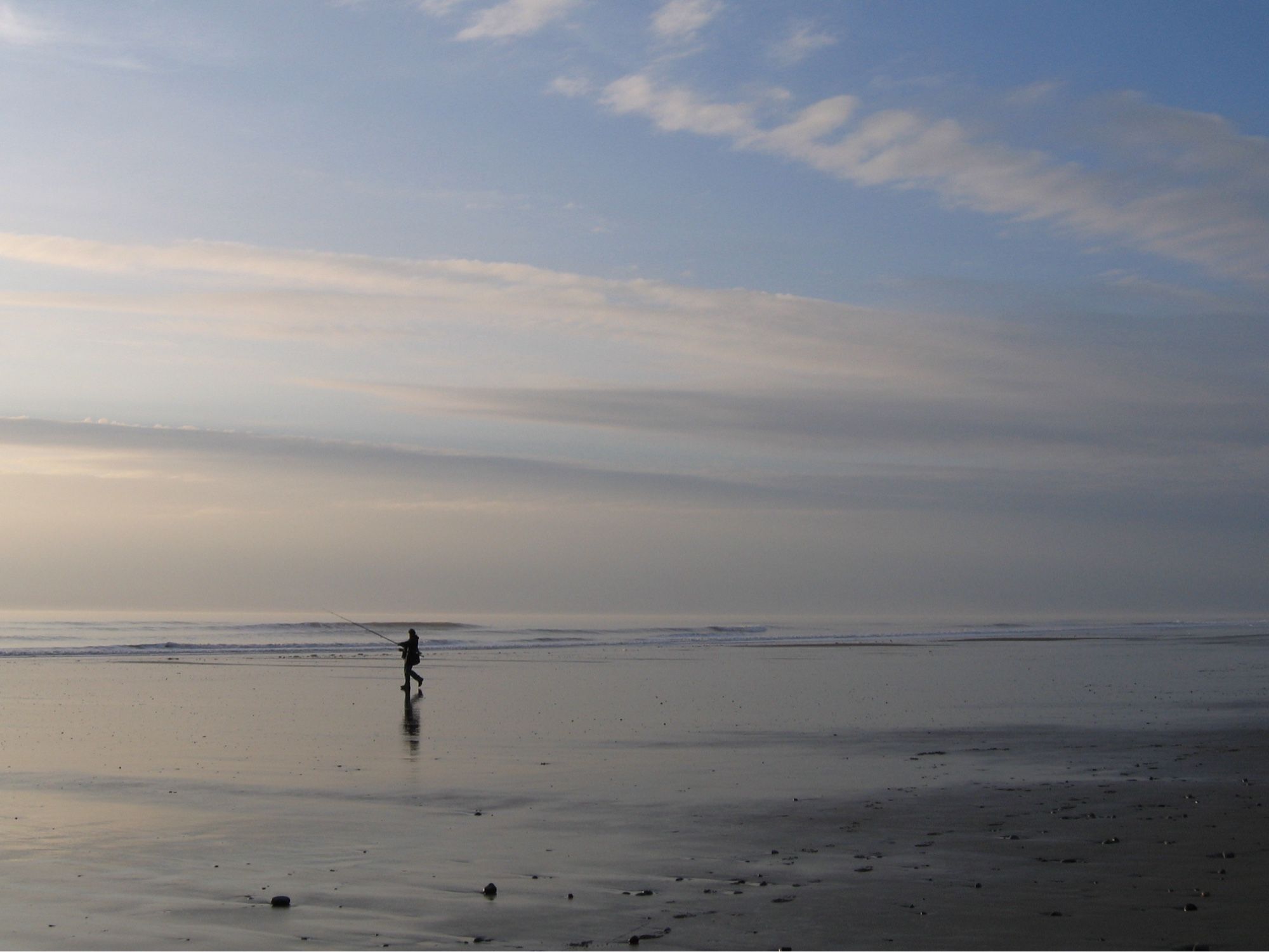 A flat beach and a flat sea, in tones of pale apricot and dusky lavender. One man, reflected in the wet sand in the middle distance, is heading towards the edge of the water