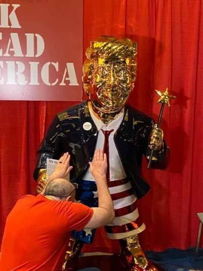 Man in red t-shirt bowing down before a golden idol of his savior.