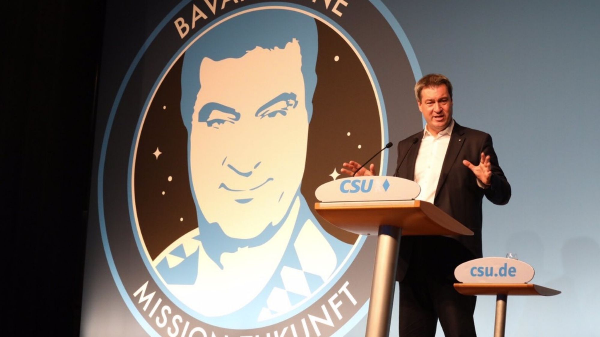 Markus Söder am Rednerpult, im Hintergrund sein Konterfei mit Sternenhintergrund, mit "Bavaria One" oben und "Mission Zukunft" umrahmt.