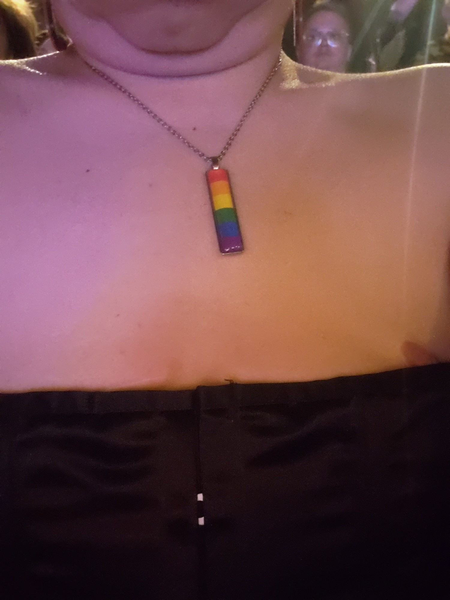 A very close up photo of a torso. There's a flat chest, nipple, and rainbow pride necklace.