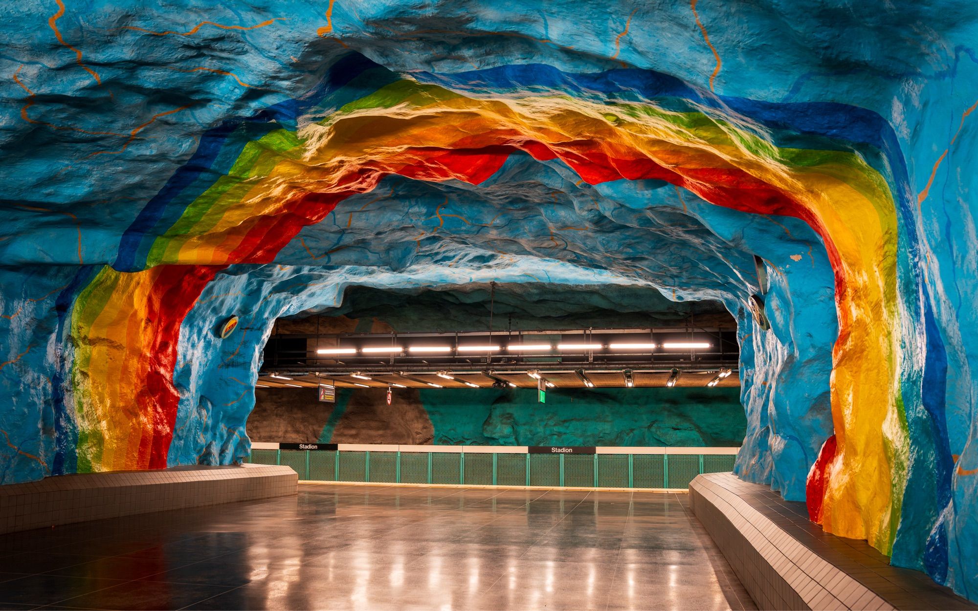 Underground metro station in Stockholm, with a multicoloured rainbow mural painted on the irregular surface.