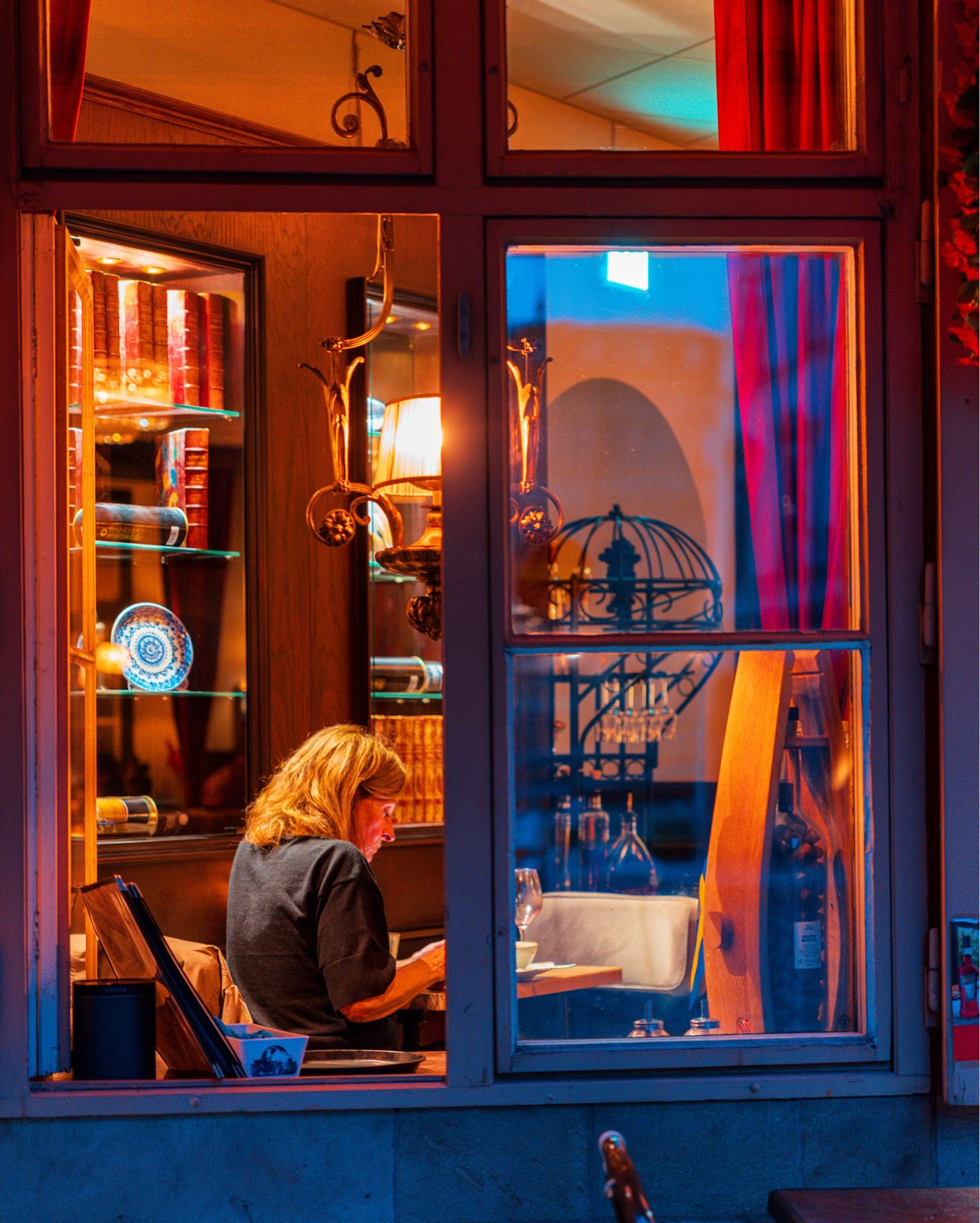 Looking into a restaurant in the evening with a lone diner minding her own business.