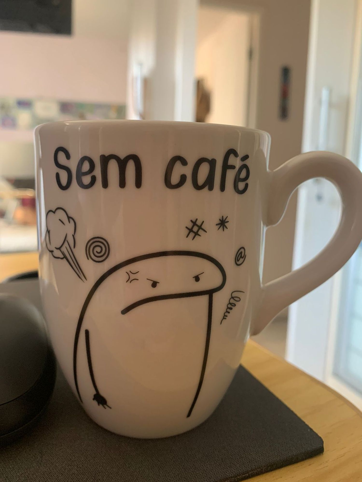 Uma foto de uma xicará de café onde tem um desenho de um bonequinho mal humorado e a legenda "sem café"