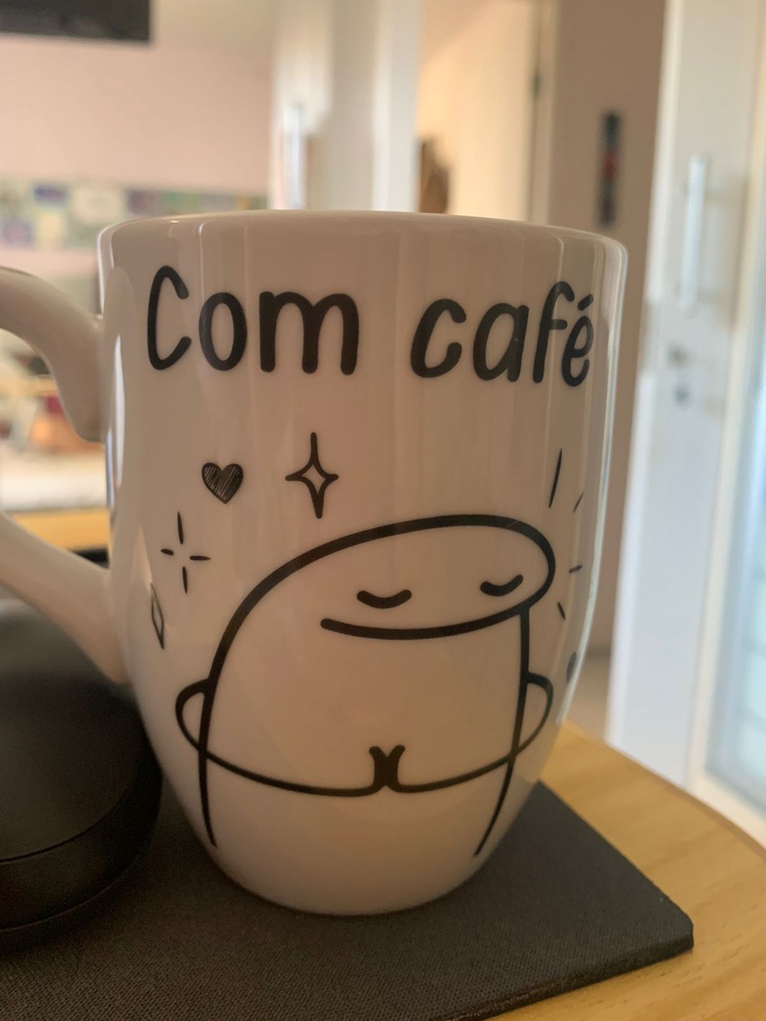 Uma foto de uma xicará de café onde tem um desenho de um bonequinho bem humorado e a legenda "com café"