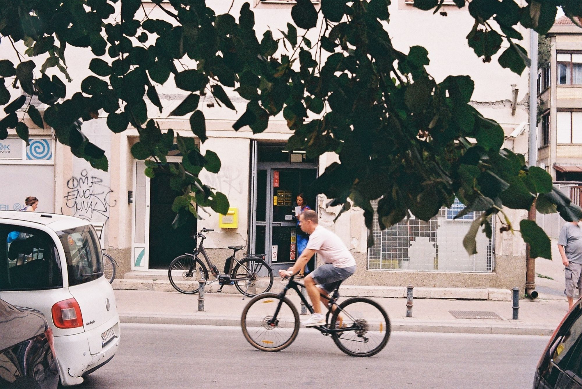 A person riding a bike in front of a post office in Novi Sad, Serbia. Leaves in the foreground.