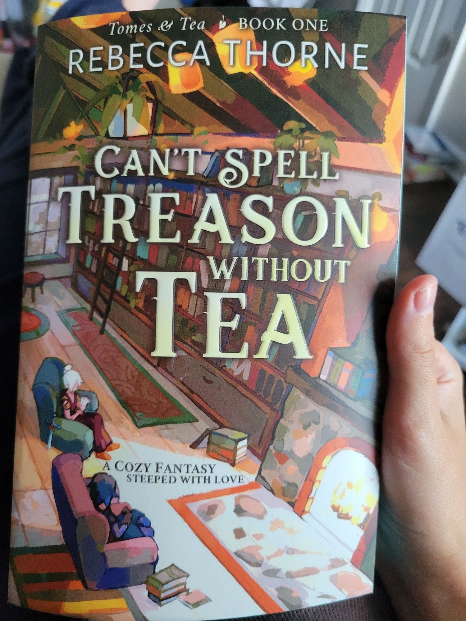 Image of the poster holding up the book 'Can't Spell Treason Without Tea' by Rebecca Thorne.