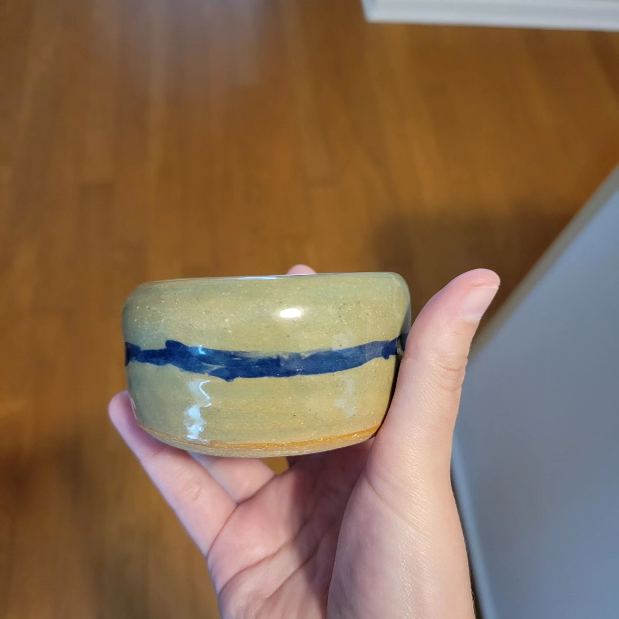 A small bowl held up with blue line across the center of the bowl and a green transparent glaze.