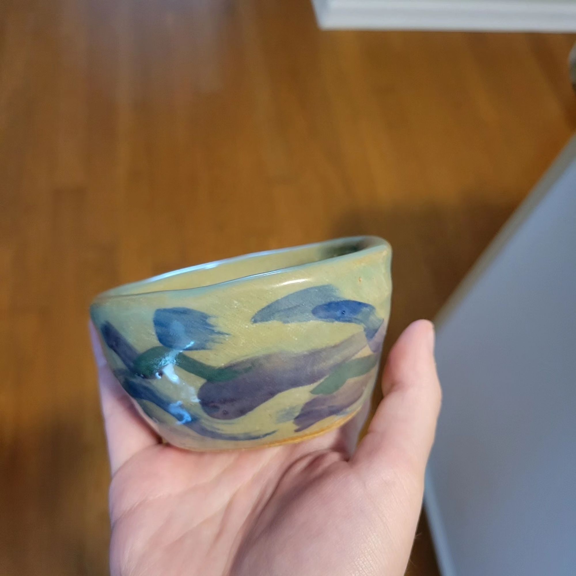 A small bowl held up with blue, dark green, and purple brush strokes on a green transparent glaze.