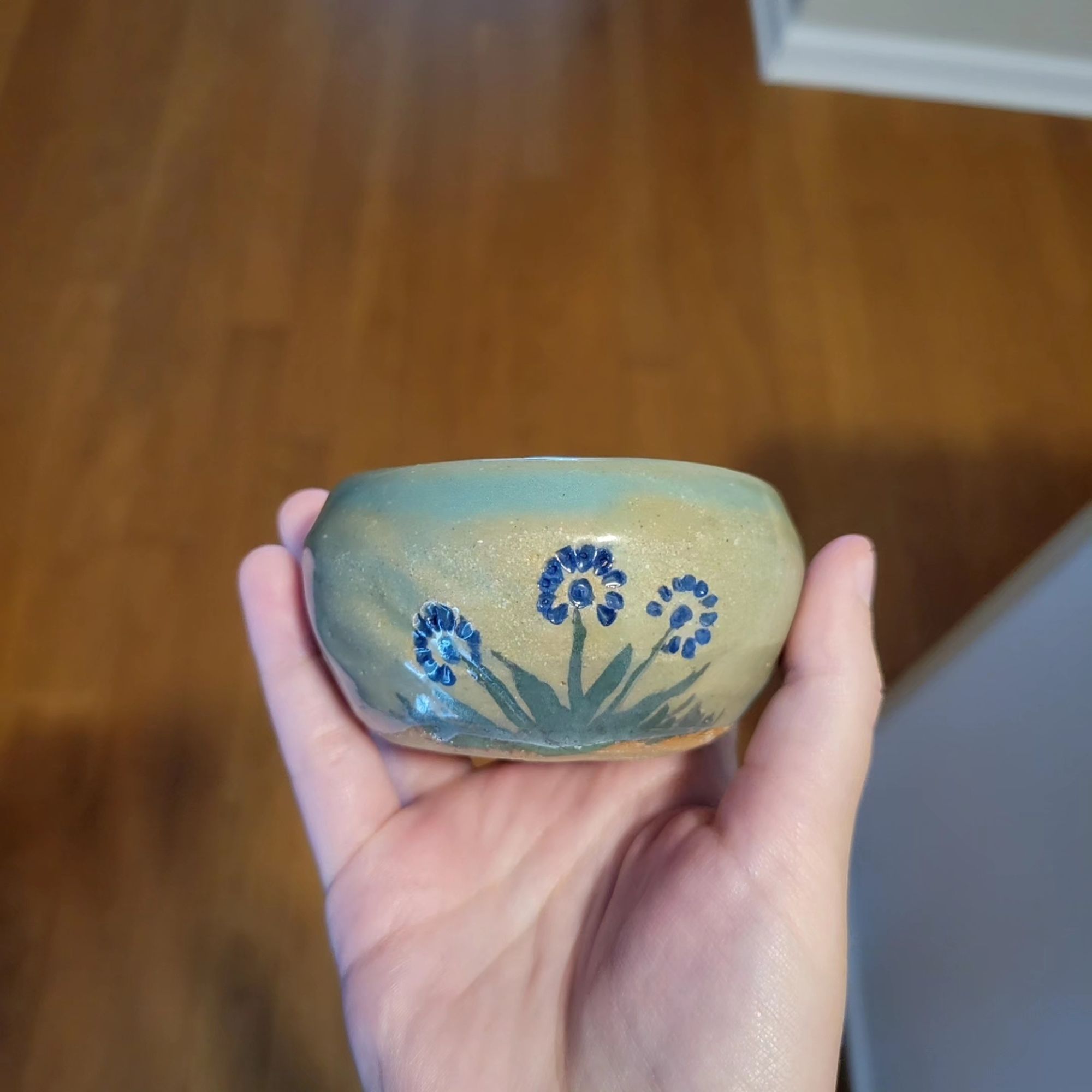 A small pottery bowl held up with three blue flowers painted on it, and green glaze.