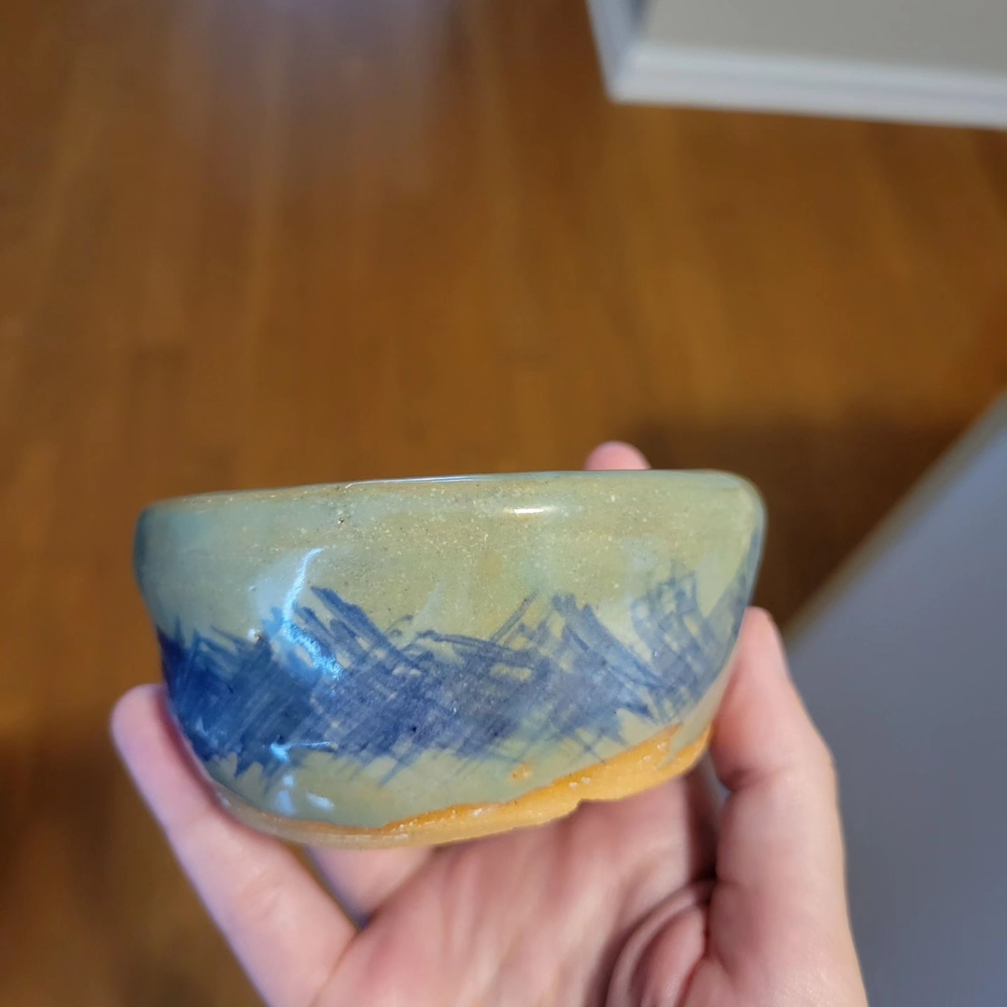 A small bowl held up with blue criss cross designs and a green transparent glaze.