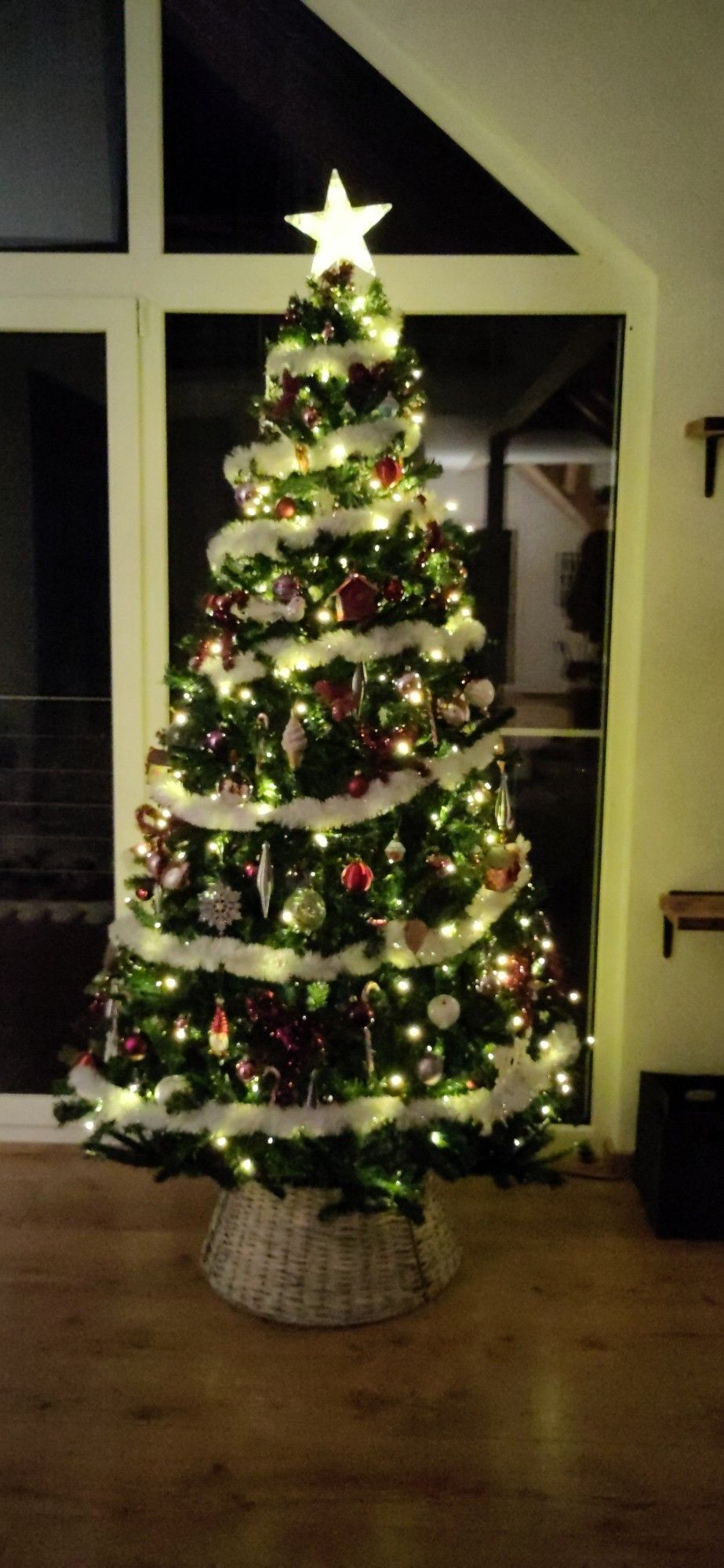 Geschmückter Weihnachtsbaum mit weißen Girlanden, pinken Kugel und einem leuchtenden stern auf der Spitze.