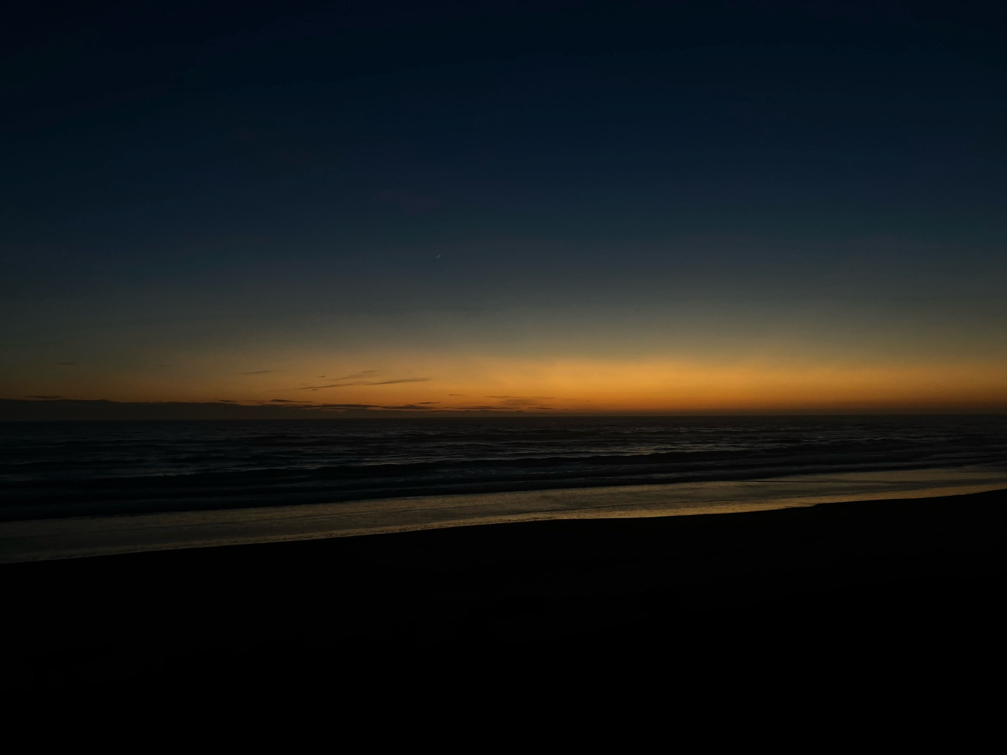 Sunset on the coastline, golden waves lapping at the dark sand mirror the warm aura of the sinking sun.