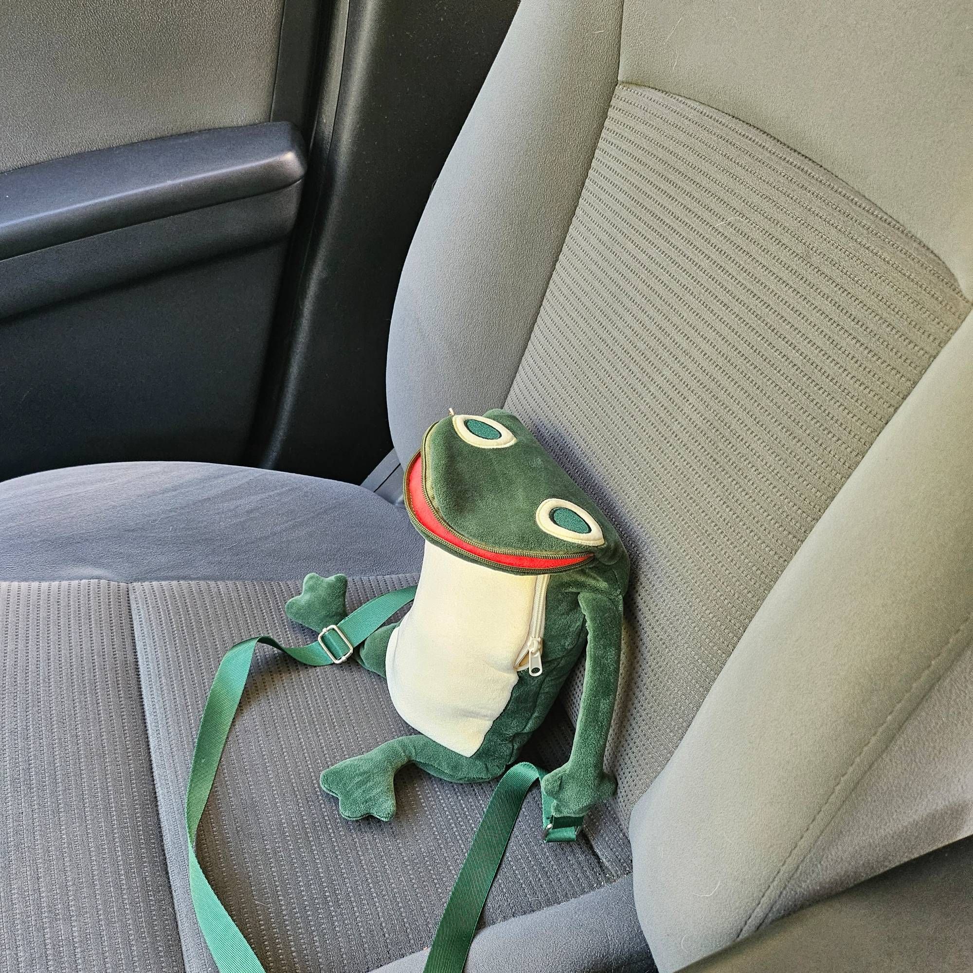 A green frog bag sitting on a gray car seat