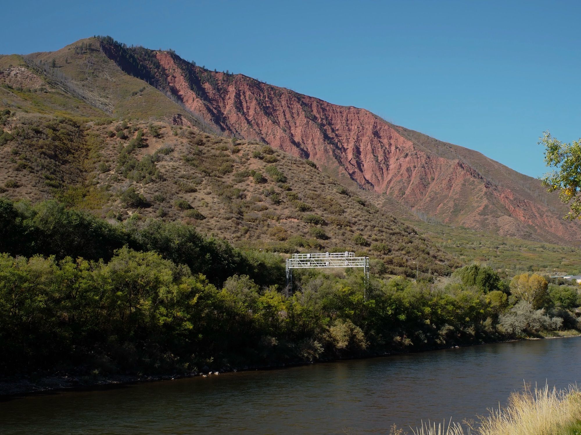 A mountain made of red stone. Its left side is covered with green foliage, but the right side is bare.