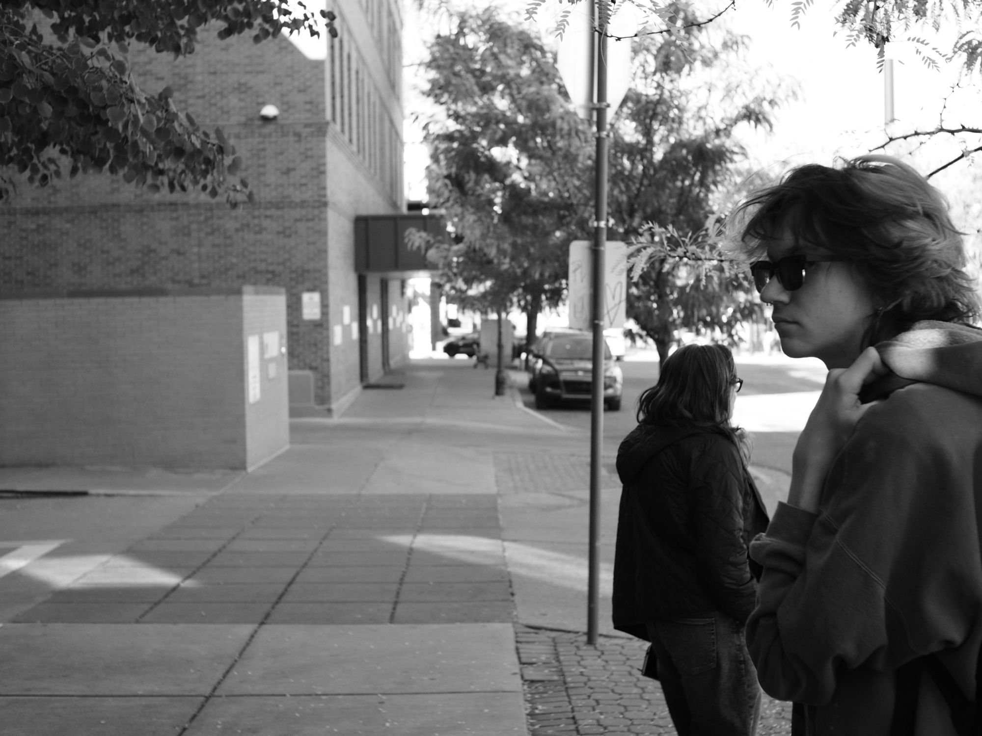 Pensive black and white shot of a young adult and woman on a side walk. They look weary.