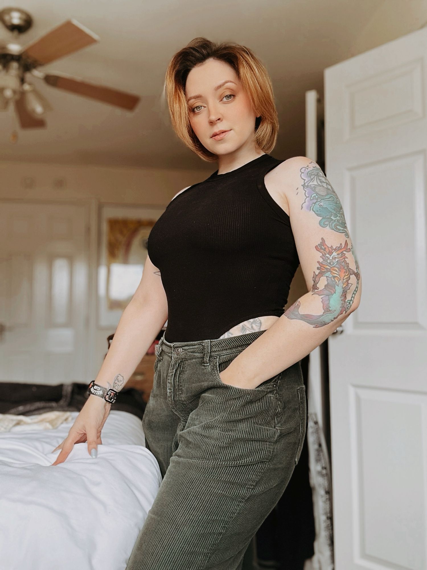 Ginger haired woman wearing sleeveless black top and green trousers. She has a tattoo of a siren and a kraken on her arm.