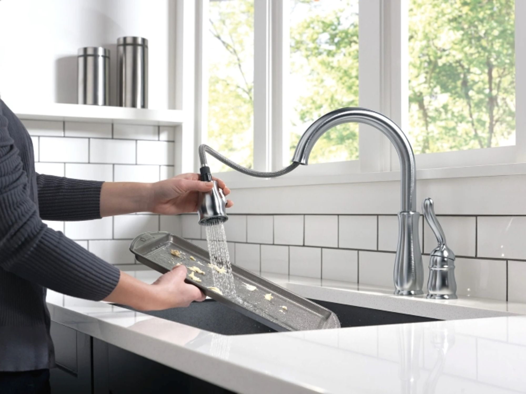 person rinsing baking sheet under kitchen tap