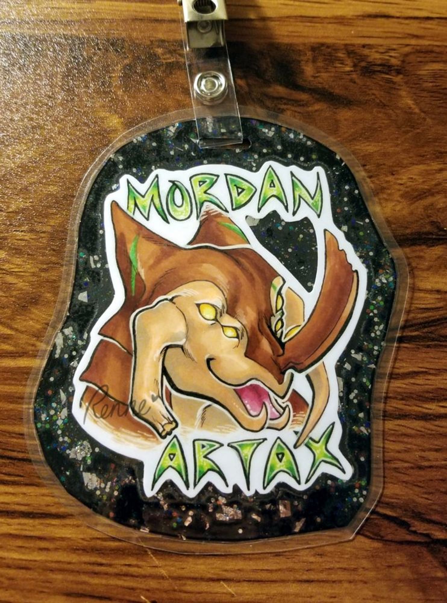 a portrait of an alien-like creature laminated and with a clip to be worn as a badge. 