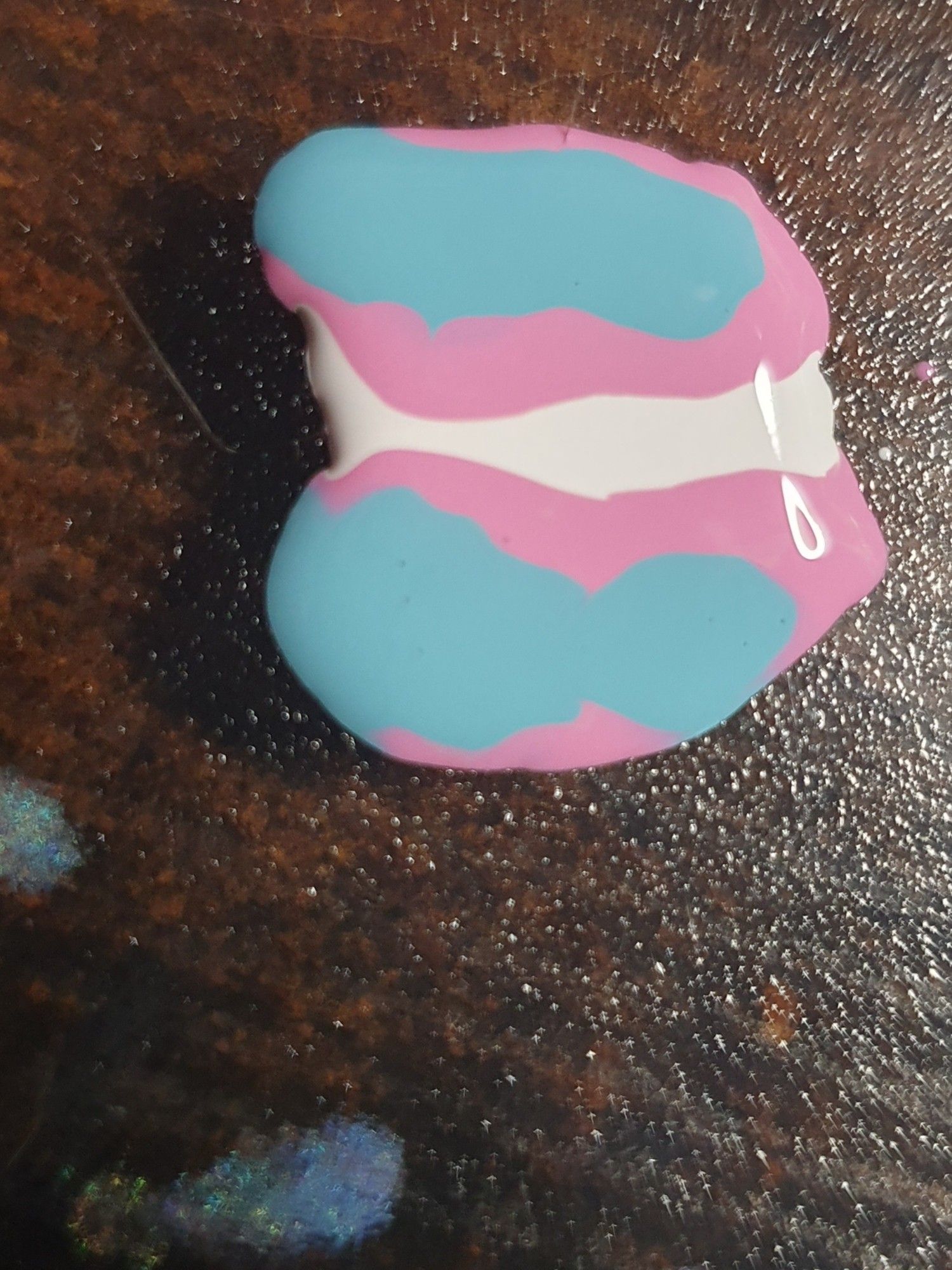 White, pink and blue nail polish puddles arranged in a Trans Flag.