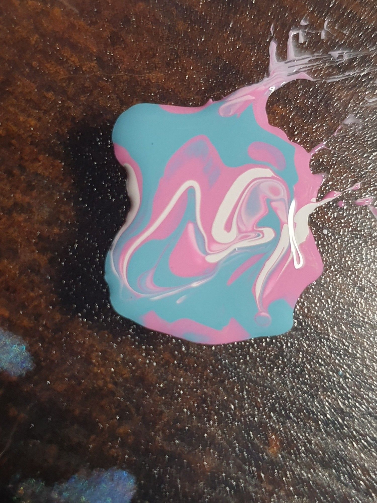 White, pink and blue nail polish puddle with the colors swirled around.