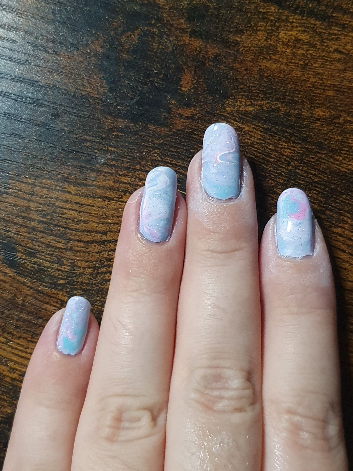 Left hand with mixed up and swirled white, pink and blue nail polish.