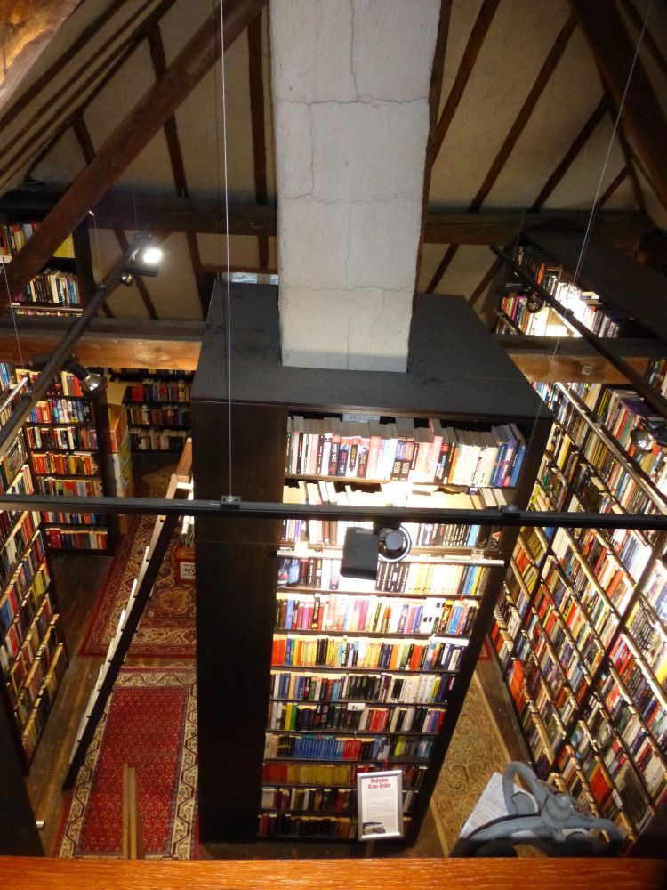 
Ein gemütliches Bibliotheksinterieur von oben, mit hohen Bücherregalen, die mit farbenfrohen Büchern gefüllt sind, die ordentlich angeordnet sind. Holzbalken und ein dekorativer Teppich sind sichtbar, zusammen mit einer zentralen Stützsäule. Die Atmosphäre ist warm und einladend, was auf einen friedlichen Leseraum hindeutet.

A cozy library interior viewed from above, featuring tall bookshelves filled with colorful books arranged neatly. Wooden beams and a decorative rug are visible, along with a central support column. The atmosphere is warm and inviting, suggesting a peaceful reading space.