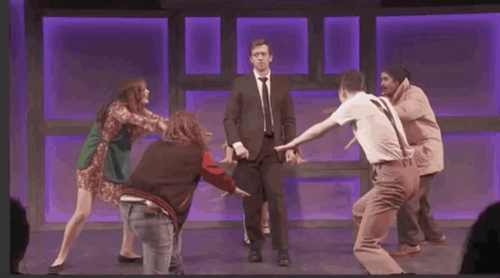 a man in a suit is surrounded by a group of people dancing on a stage