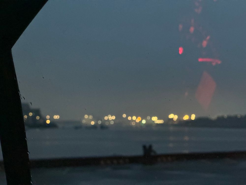 A blurry photo of river after sunset. Crane lights bokeh into the background, and the dashboard light is reflected over the image.