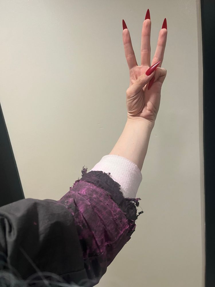 My left arm, wearing a wraparound bandage and a sawed-off sleeve covered in dried magenta gouache paint, simulating blood.