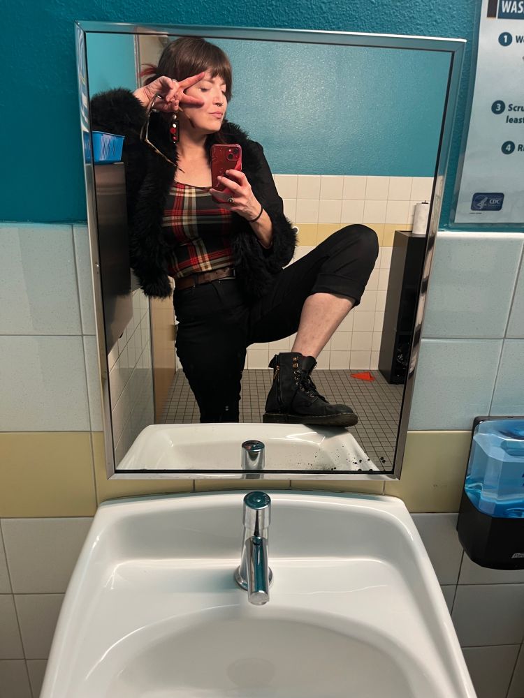 i’m wearing black cuffed jeans, black boots, a plaid shirt, and a black jacket with faux fur frills on the cuffs and collar