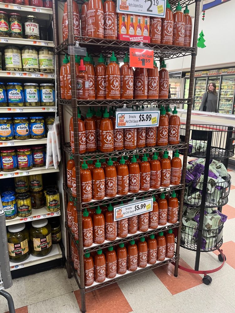 A six-shelf high grocery store rack completely filled with large bottles of Huy Fong sriracha hot sauce