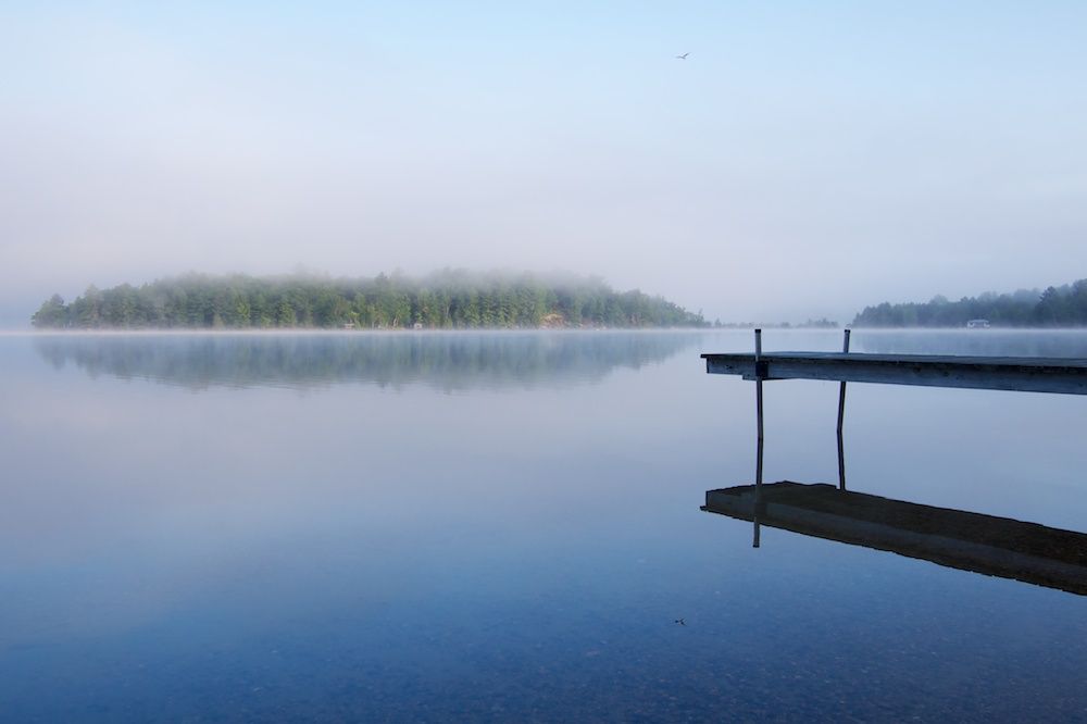 A lake in the mist, with two land masses in the distance, and a section of a boat dock at the right of the scene