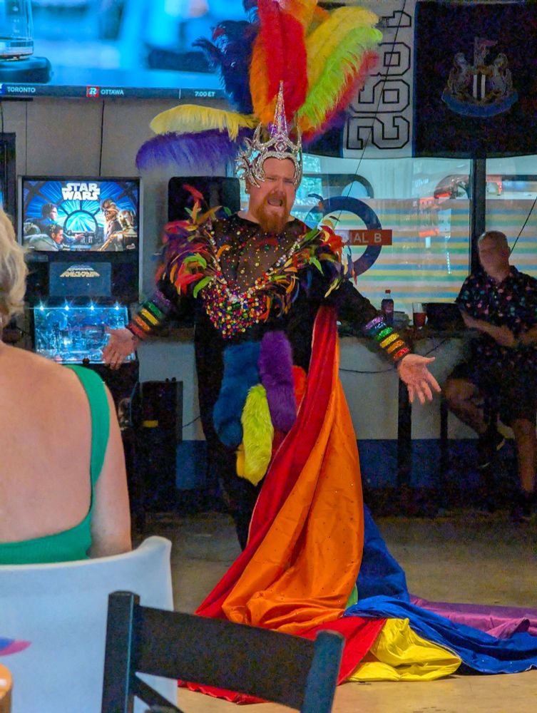 A man wearing a bright, colorful costume poses in a room filled with lively decor and vibrant colors.